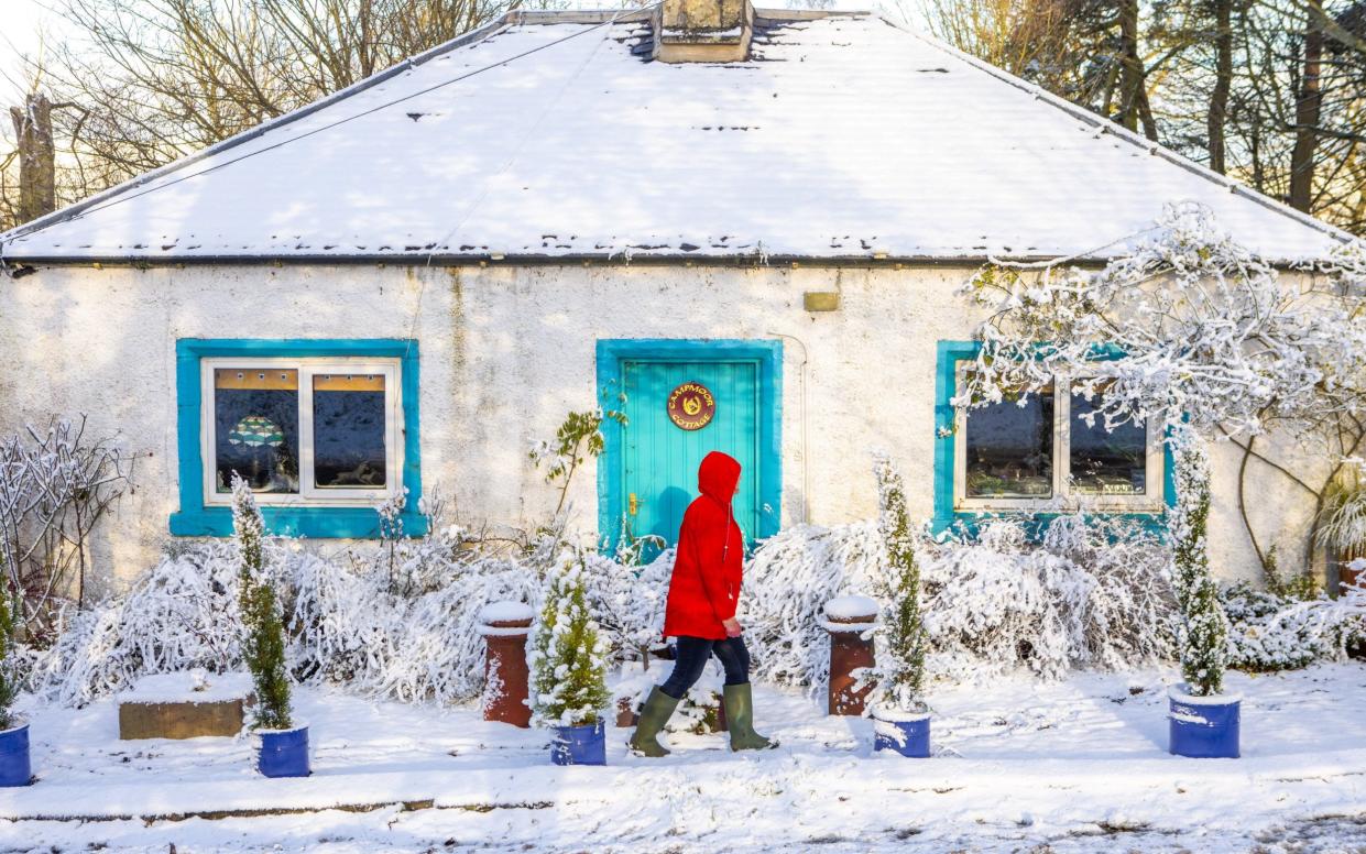 A woman in red coat walks past a snow-covered cottage near Duns in the Scottish Borders