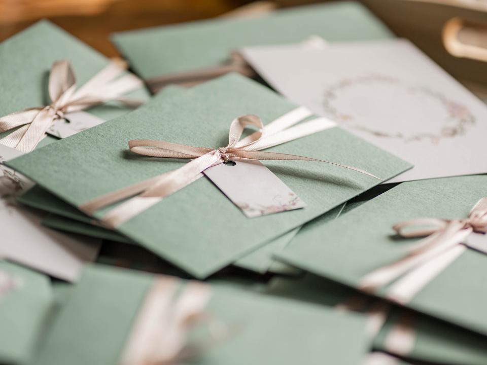 a pile of green envelopes with ribbons on them, wedding invitations