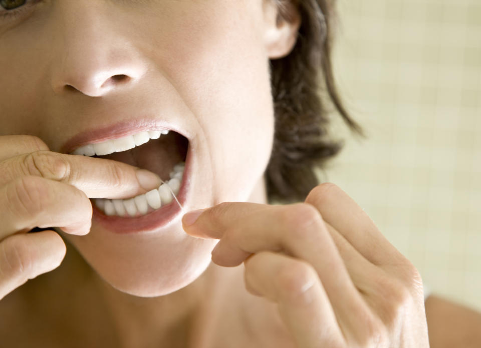 Close-up of a person flossing their teeth with a focused expression on their face