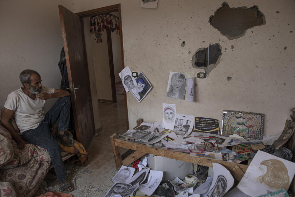 Adnan, father of Duniana al-Amour sits among her drawings in her damaged room which was hit by an Israeli strike, east of Khan Yunis, in the southern Gaza Strip, Monday, Aug. 10, 2022. Al-Amour, a 22-year-old Palestinian woman who had retreated into her artistic pursuits during Gaza's past wars was among the first people killed by Israeli strikes in the latest round of violence. Shrapnel tore through her bedroom during Israel’s surprise opening salvo last Friday, hours before militants fired any rockets. (AP Photo/Fatima Shbair)