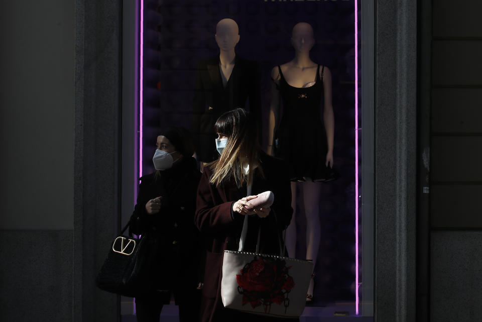 Women wearing a face mask walk past a fashion store's front window in Monte Napoleone shopping street during the Fashion Week, in Milan, Italy, Wednesday, Feb. 24, 2021. (AP Photo/Antonio Calanni)