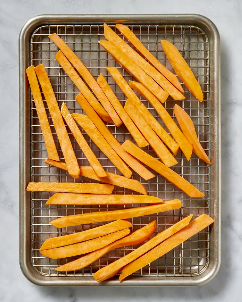 Overhead view of unbaked sweet potato fries on a cooling rack in a baking sheet.