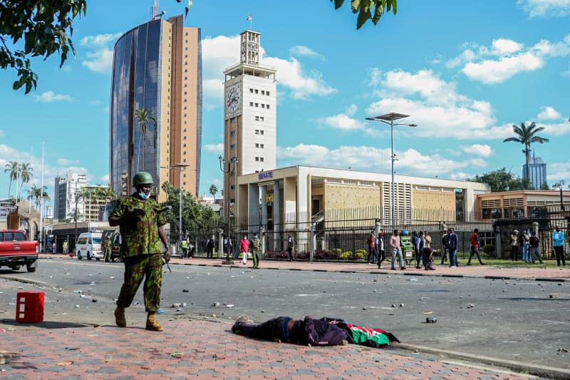 A police officer passes near a body of a demonstrator on a sidewalk near the Parliament building, during a demonstration against proposed tax hikes in Kenya. Boniface Muthoni/SOPA Images via ZUMA Press Wire/dpa