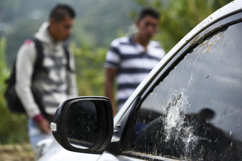 People gather around a car riddled by bullets on the road leading to Tacueyo, in southwest Colombia, Wednesday, Oct. 30, 2019. Five indigenous leaders of the Tacueyo reservation were killed late Tuesday when the vehicles they were traveling in were ambushed by gunmen the government says are part of a dissident front of Revolutionary Armed Forces of Colombia. (AP Photo/Christian Escobar Mora)