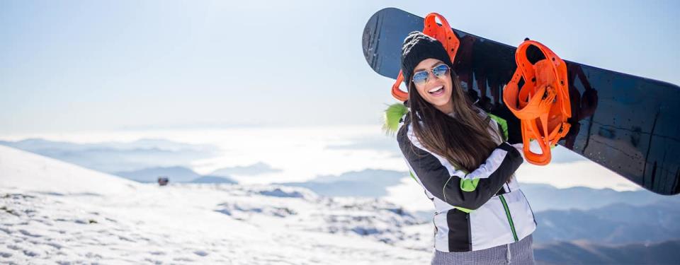 woman carrying snowboard smiling winter mountains sunny sky inbody