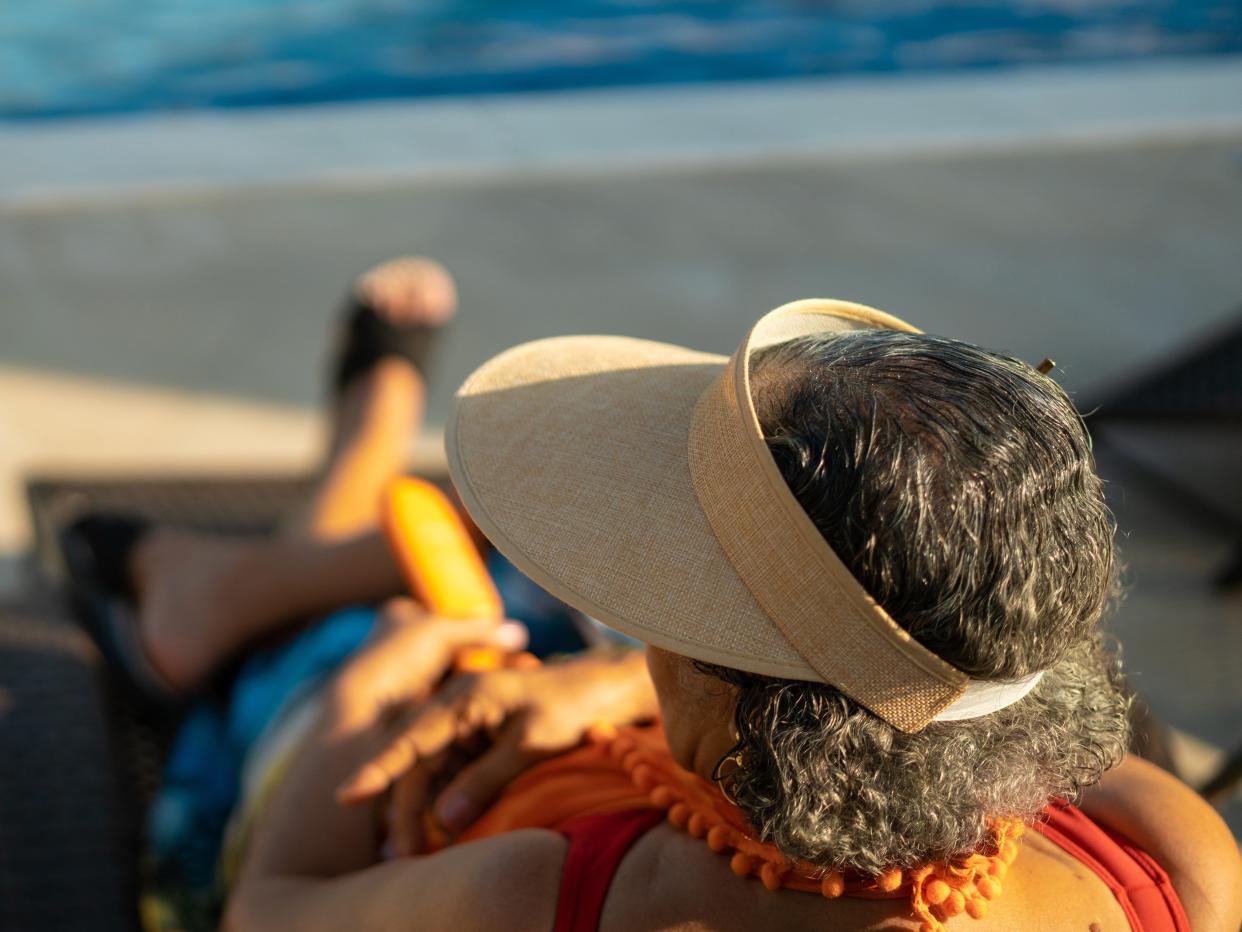 A view from behind of a woman wearing a sun visor facing the pool.