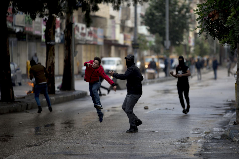 A Palestinian demonstrator hurls stones at Israeli troops during a protest in the West Bank city of Hebron, Monday, Dec. 9, 2019. Palestinian residents held a general strike to protest an Israeli plan to build a new Jewish neighborhood in the heart of the West Bank's largest city. (AP Photo/Majdi Mohammed)