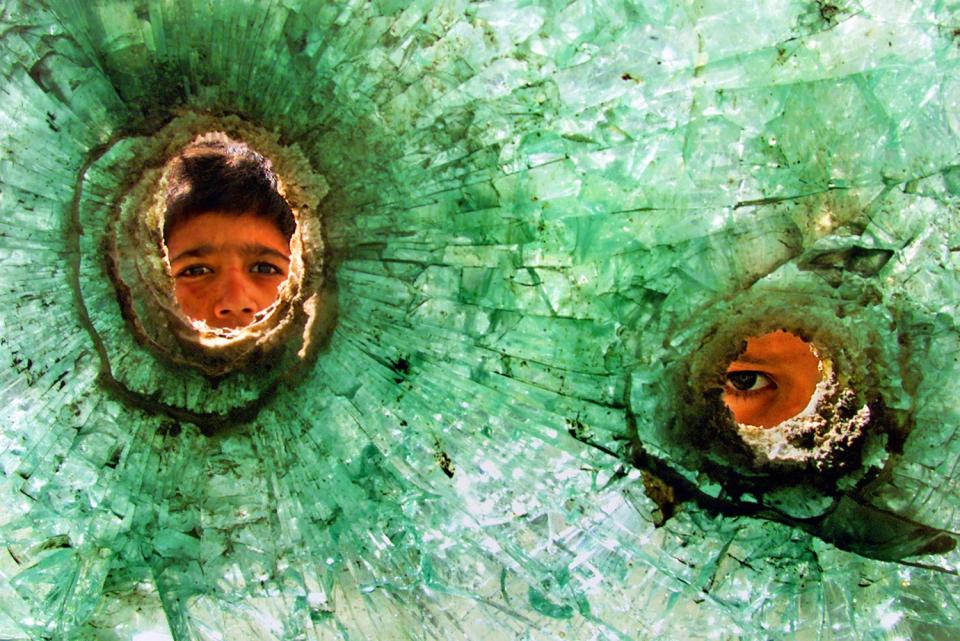 Two boys faces seen through bullet holes in shattered glass