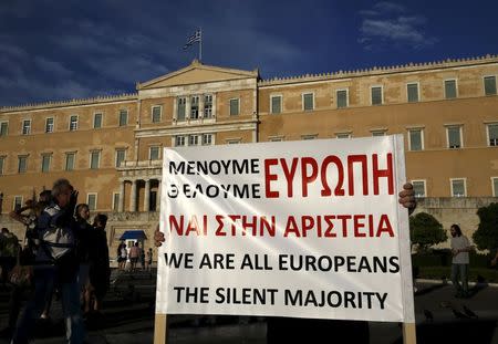 A protester holds a placard as people gather at the entrance of the Greek parliament, during a rally calling on the government to clinch a deal with its international creditors and secure Greece's future in the Eurozone, in Athens June 18, 2015. REUTERS/Yannis Behrakis