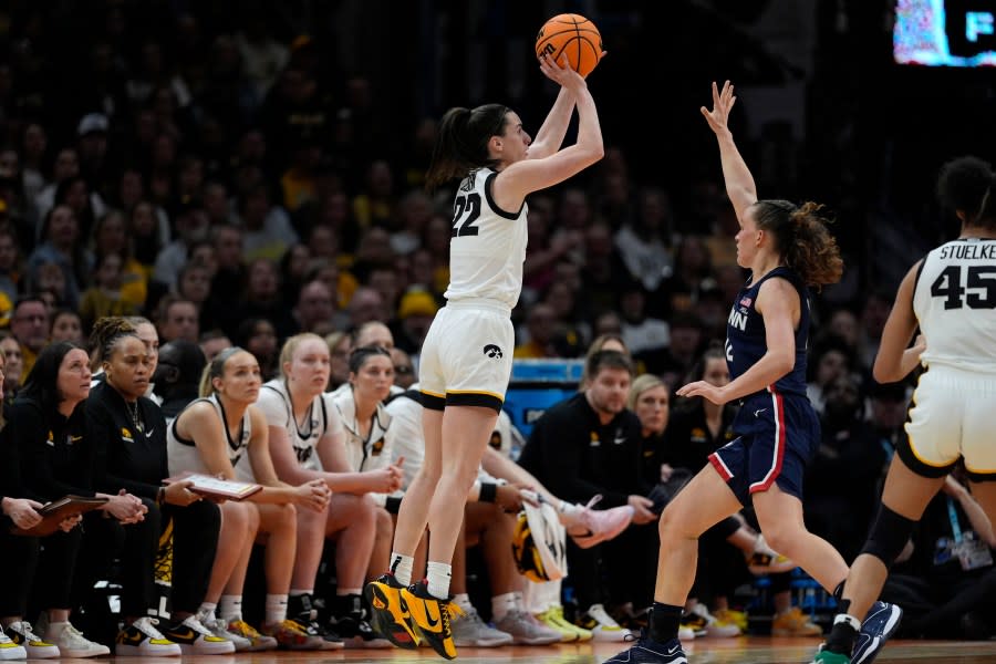 Iowa guard Caitlin Clark (22) shoots a three-point basket over UConn guard Ashlynn Shade, right, during the second half of a Final Four college basketball game in the women's NCAA Tournament, Friday, April 5, 2024, in Cleveland. (AP Photo/Carolyn Kaster)