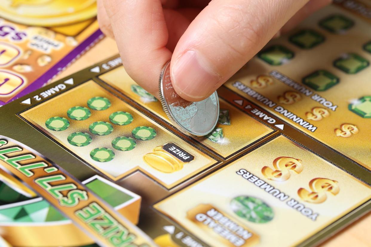 Closeup of fingers holding a quarter, scratching off a new lottery ticket with another scratch-off lottery ticket to the left