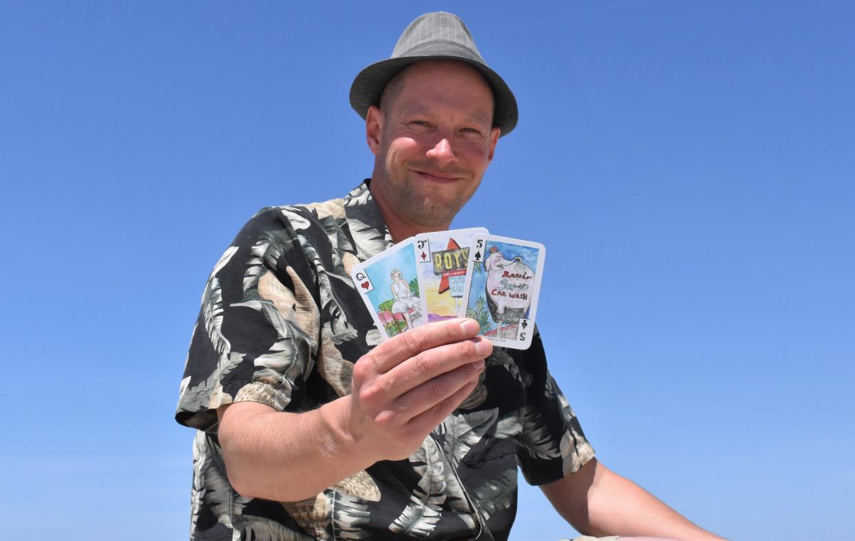 Artist Aaron Trotter holds a deck of cards illustrating symbols and landmarks of Palm Springs.
