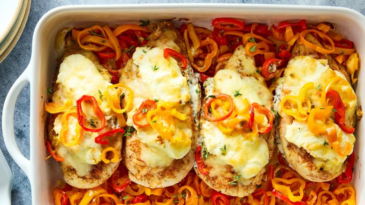 chicken breasts in a casserole dish baked over peppers and topped with cheese
