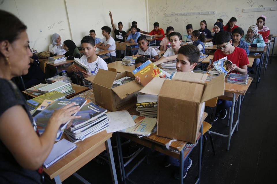 Palestinian refugee students receive new studying books inside their classroom, during the first day of a new school year, at one of the UNRWA schools, in Beirut, Lebanon, Monday, Sept. 3, 2018. The United Nations' Palestinian relief agency celebrated the start of the school year in Lebanon on Monday, managing to open its schools on schedule despite a multi-million dollar budget cut on the heels of U.S. President Donald Trump's decision to stop funding to the agency. (AP Photo/Hussein Malla)