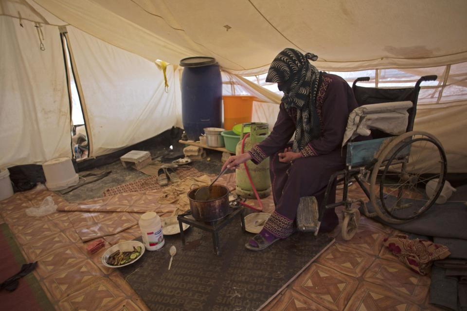 In this Thursday April 17, 2014 photo, Ghasibeh Kasabneh, 46, prepares food for the family, inside her tent at Zaatari Syrian refugee camp, near the Syrian border in Jordan. Zaatari is the region's largest camp for Syrian refugees. (AP Photo/Khalil Hamra)