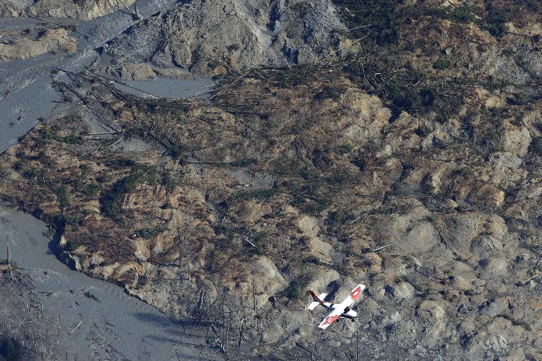 A Civil Air Patrol plane flies over the massive mudslide that killed at least eight people and left dozens missing as shown in this aerial photo, Monday, March 24, 2014, near Arlington, Wash. The search for survivors grew Monday raising fears that the death toll could climb far beyond the eight confirmed fatalities. (AP Photo/Ted S. Warren)