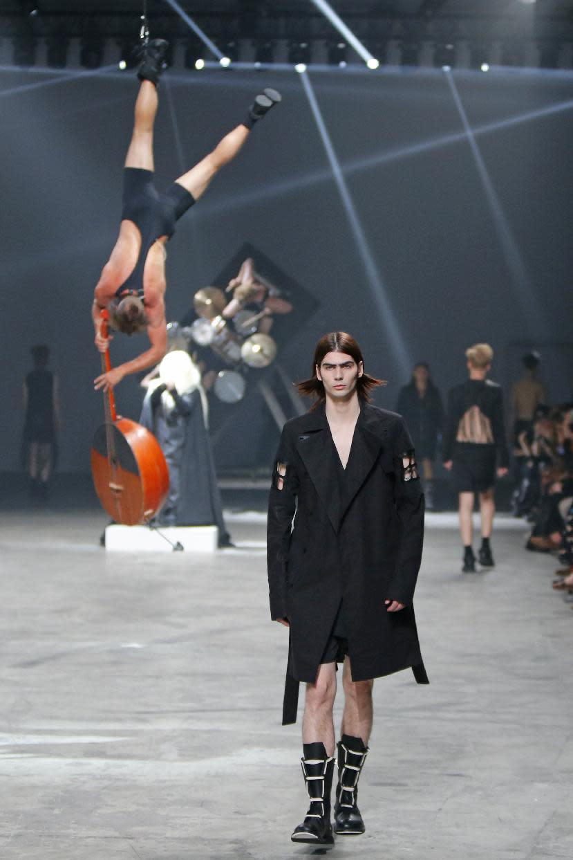 A model wears a creation by fashion designer Rick Owens as part of his men's fashion Spring-Summer 2014 collection, presented Thursday, June 27, 2013 in Paris, as Estonian metal/punk band Winny Puhh perform live, suspended by their feet, rear left . (AP Photo/Francois Mori)