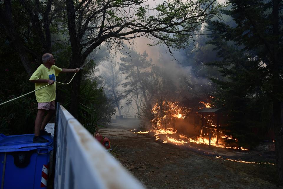 A man drops water to burning trees during a wildfire in Adames area, northern Athens, Greece, Tuesday, Aug. 3, 2021. Hundreds of residents living near a forest area north of Athens fled their homes. (AP Photo/Michael Varaklas)