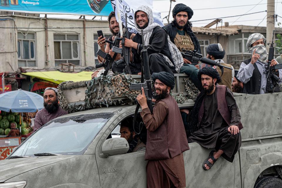 Taliban fighters hold weapons as they ride in a convoy to celebrate their victory day near the former U.S. Embassy building in Kabul, August 15, 2022. / Credit: WAKIL KOHSAR/AFP/Getty