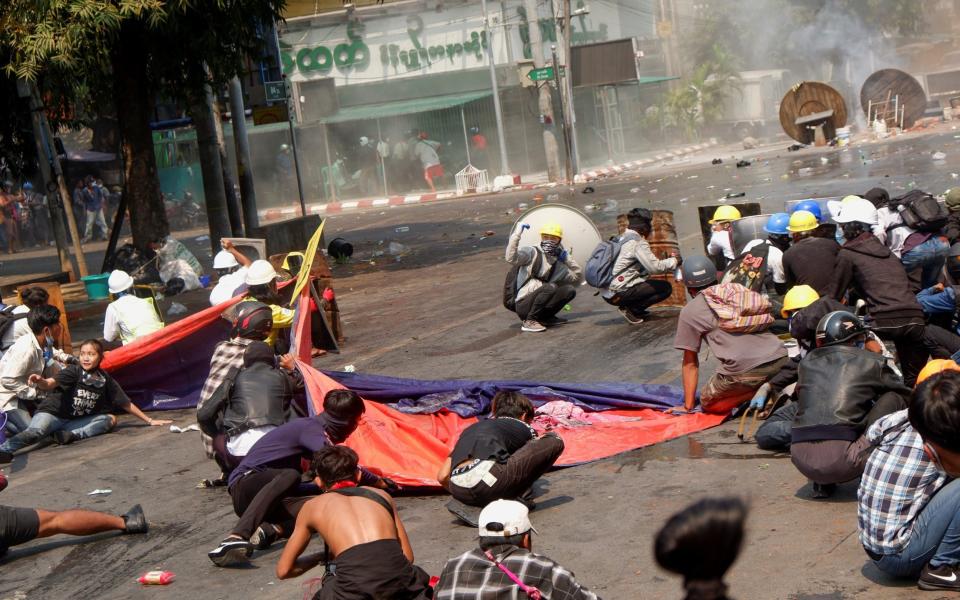 Protesters lie on the ground after police open fire to disperse an anti-coup protest - REUTERS