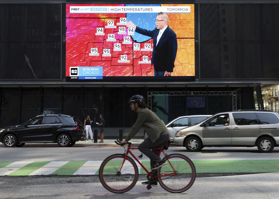 A bicyclist rides past a screen airing a news channel weather segment forecasting an upcoming heat wave, Tuesday, Aug. 22, 2023, at Daley Plaza in Chicago. Scorching heat affecting nearly 100 million people across a huge swath of the U.S. is sending schools, outdoor workers and organizers of open-air events scrambling to adjust. (John J. Kim/Chicago Tribune via AP)