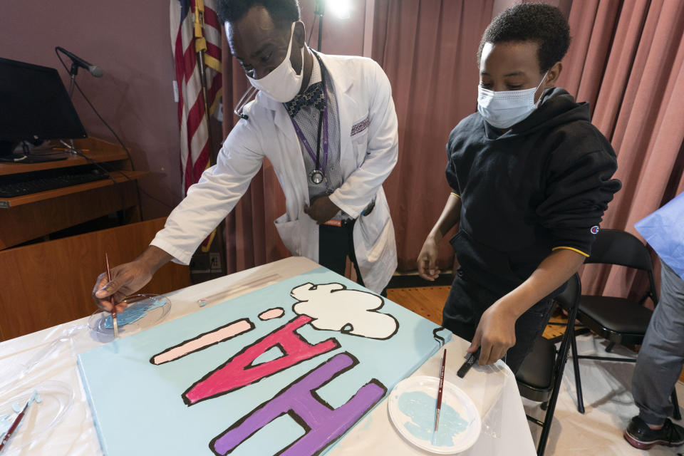 Pediatric resident Dr. Salome Wiredu, left and Jesse McCarty, 14, paint a panel of a "Peanuts" mural that will be placed in the outpatient pediatric floor of One Brooklyn Health at Brookdale Hospital, Thursday, Oct. 1, 2020, in the Brooklyn borough of New York. The beloved comic marks its 70th anniversary this week with new lesson plans, a new TV show and a philanthropic push that includes donating "Peanuts" murals for kids to paint in 70 children's hospitals around the globe, from Brooklyn to Brazil.(AP Photo/Mary Altaffer)