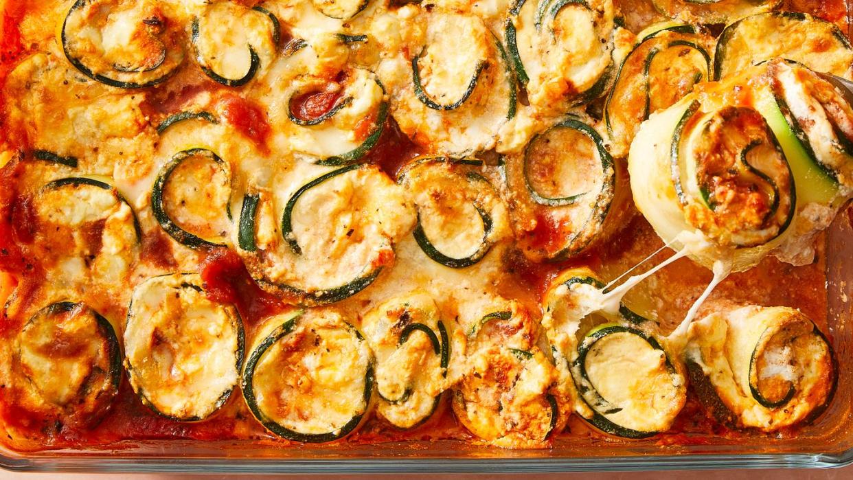 zucchini slices rolled up around cheese with sauce in a casserole dish