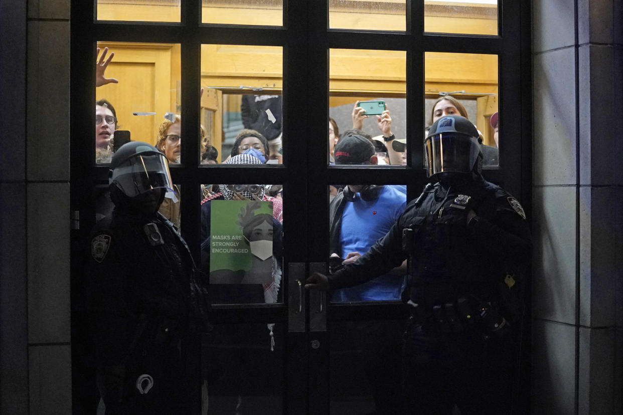 NYPD officers stand outside the doors of Hamilton Hall as protesters are seen inside.