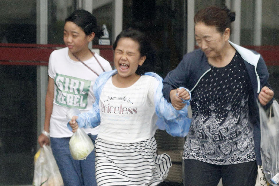 A girl grimes against a strong wind brought by Typhoon Tapah in Nakatane, Kogoshima prefecture, southwestern Japan, Sunday, Sept. 22, 2019. The powerful typhoon was heading northeast to Japan's main island of Honshu on Sunday after lashing parts of the country's southern islands with heavy rains and winds that caused flooding and some minor injuries. (Kyodo News via AP)