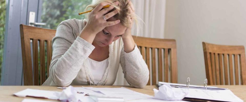 Woman sits at table with head in hands, looking at pile of bills