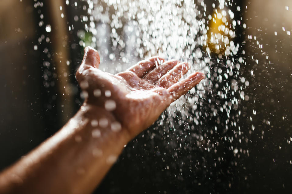 A man's hand in a spray of water in the sunlight against a dark background