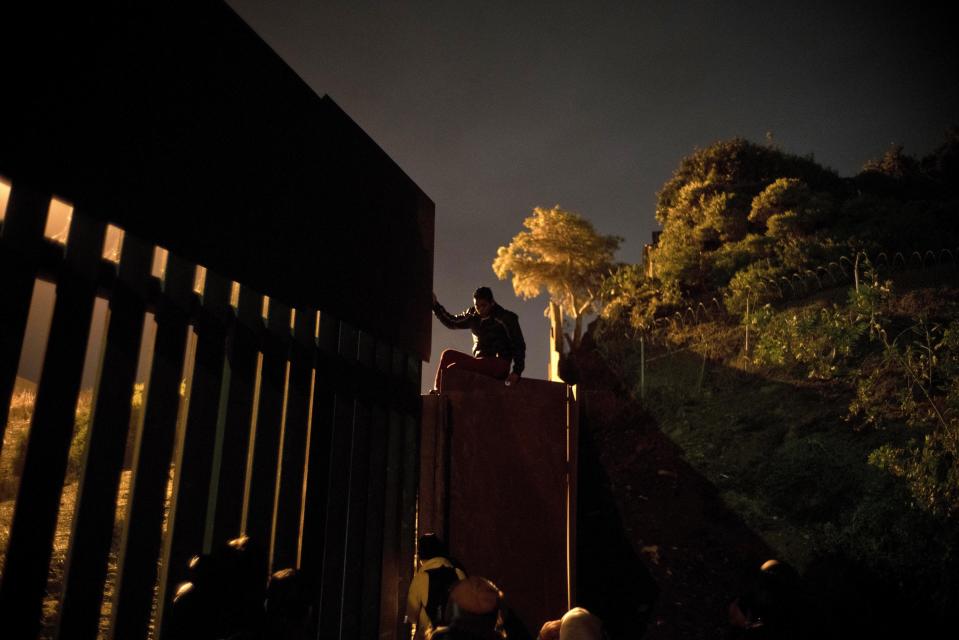 A Honduran migrant climbs the border wall separating Tijuana, Mexico and San Diego, before crossing to the U.S with his son in Tijuana, Mexico, Thursday, Nov. 29, 2018. Aid workers and humanitarian organizations expressed concerns Thursday about the unsanitary conditions at the sports complex in Tijuana where more than 6,000 Central American migrants are packed into a space adequate for half that many people and where lice infestations and respiratory infections are rampant. (AP Photo/Ramon Espinosa)