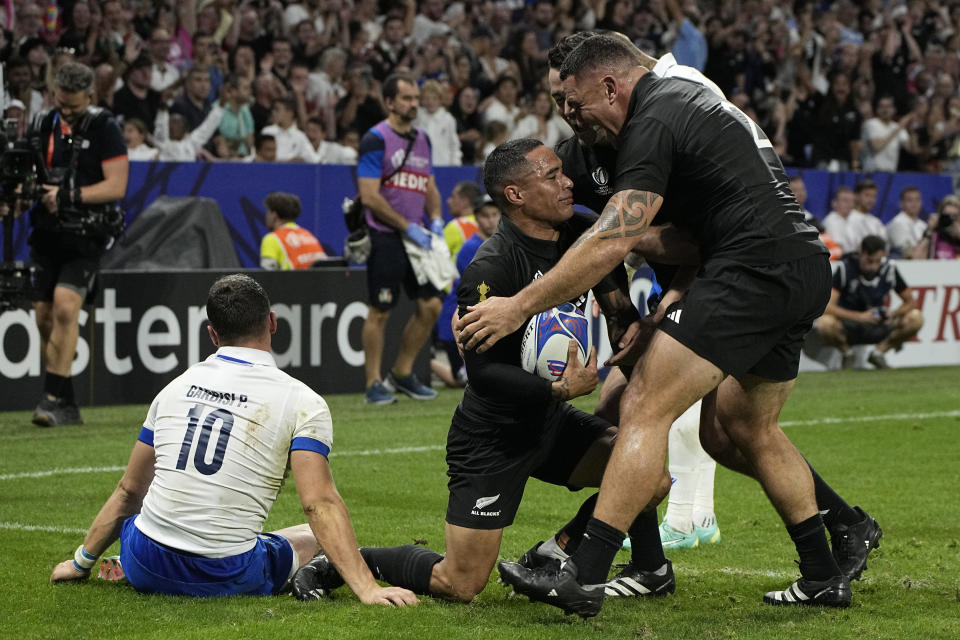 New Zealand's Aaron Smith, center, is congratulated by teammates after scoring as Italy's Paolo Garbisi sits on the pitch during the Rugby World Cup Pool A match between New Zealand and Italy at the OL Stadium in Lyon, France, Friday, Sept. 29, 2023. (AP Photo/Laurent Cipriani)