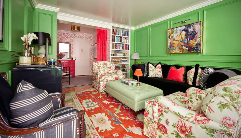 Green living room with wainscoting, matching floral chairs, and a mint green tufted ottoman as coffee table.