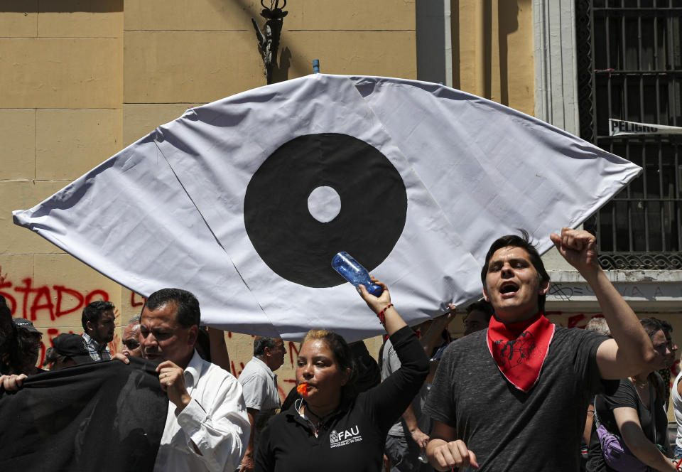 Anti-government demonstrators shout slogans against Chilean police, with a banner representing a eye, in reference of the more than 200 people who have been shot in the eyes with birdshot during the ongoing protests, in Santiago, Chile, Tuesday, Nov. 12, 2019. Students in Chile began protesting nearly a month ago over a subway fare hike. The demonstrations have morphed into a massive protest movement demanding improvements in basic services and benefits, including pensions, health, and education. (AP Photo/Esteban Felix)