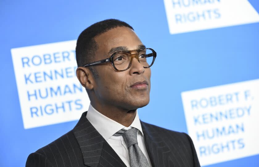 Man, don lemon, looking toward right, wearing thick-rimmed glasses and black suit with gray tie