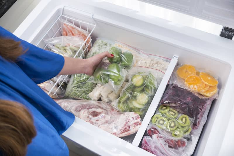 A woman putting green bell peppers into fridge.