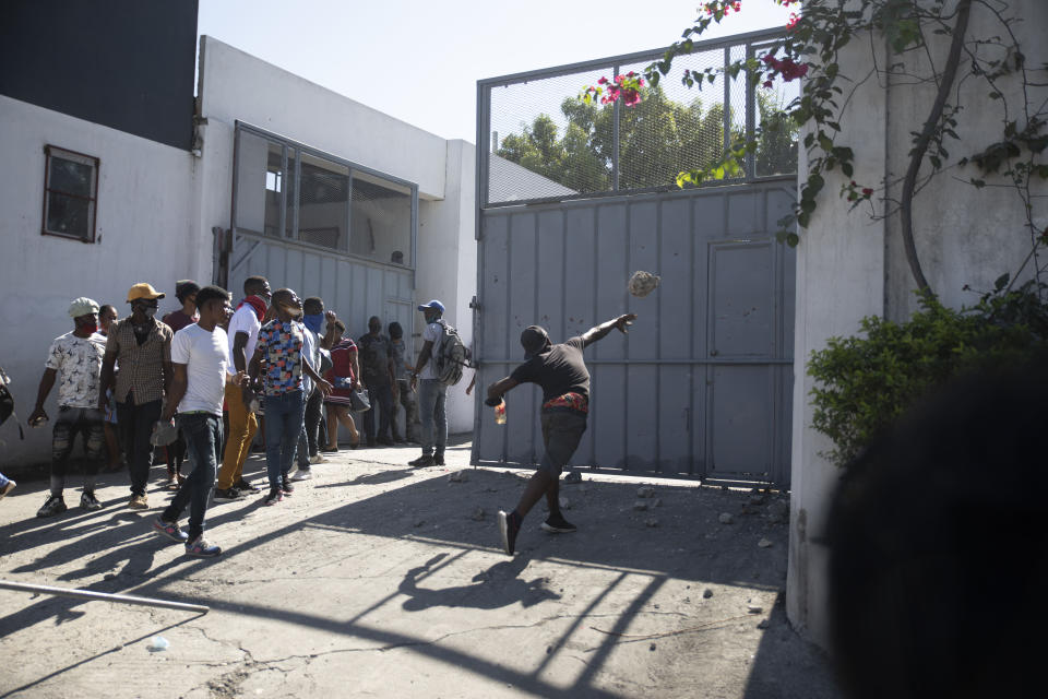 A protester throws a rock at a factory, during a march and protest by workers demanding a salary increase in Port-au-Prince, Haiti, Wednesday, Feb. 23, 2022. It is the first day of a three-day strike organized by factory workers who also shut down an industrial park earlier this month to protest pay. (AP Photo/Odelyn Joseph)