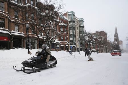 A snowmobile pulls a man on snow board on Newbury Street in Boston, Massachusetts following a winter storm February 15, 2015. REUTERS/Brian Snyder