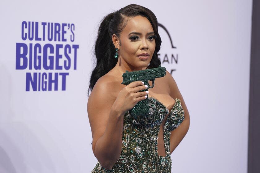 Angela Simmons showing off a bedazzled green purse shaped like a handgun while wearing a sleeveless green gown