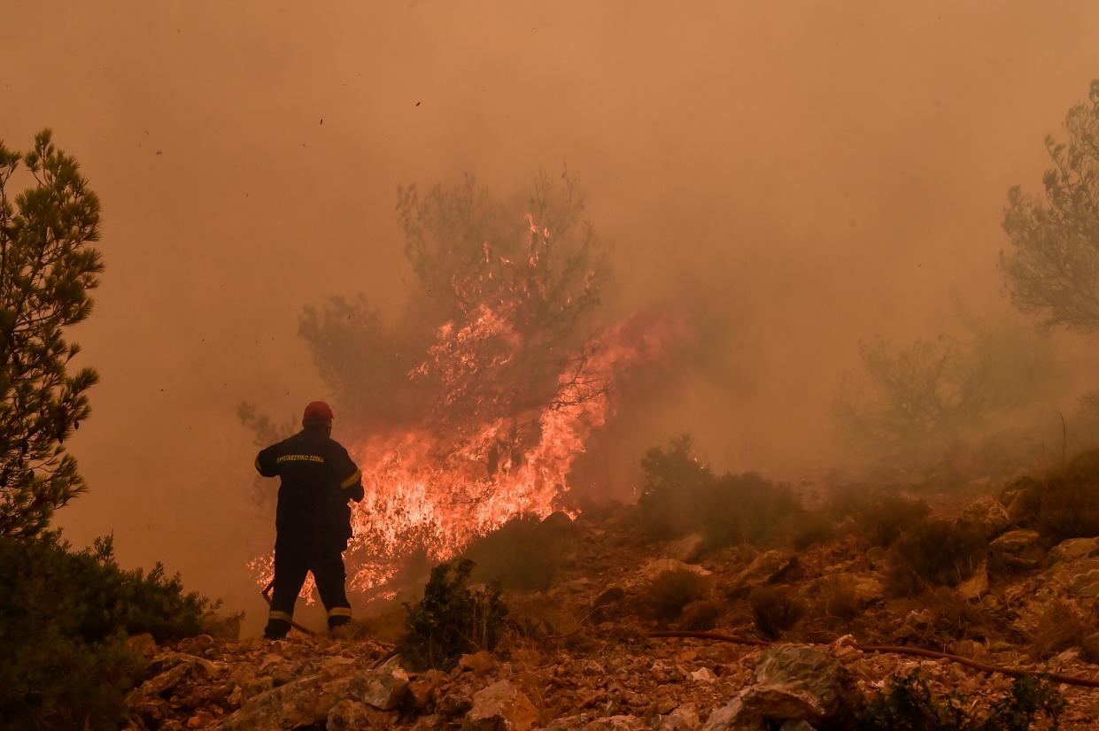 Locals help a firefighter as they try to extinguish a wildfire burning near the village Vlyhada near Athens (Getty Images)