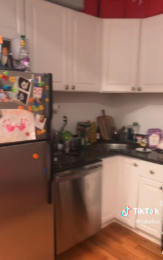 Julia's kitchen countertops are filled with everyday culinary essentials like a cutting board and cleaning products. There is a cute painted hand piece of art that her son like made attached to the freezer door