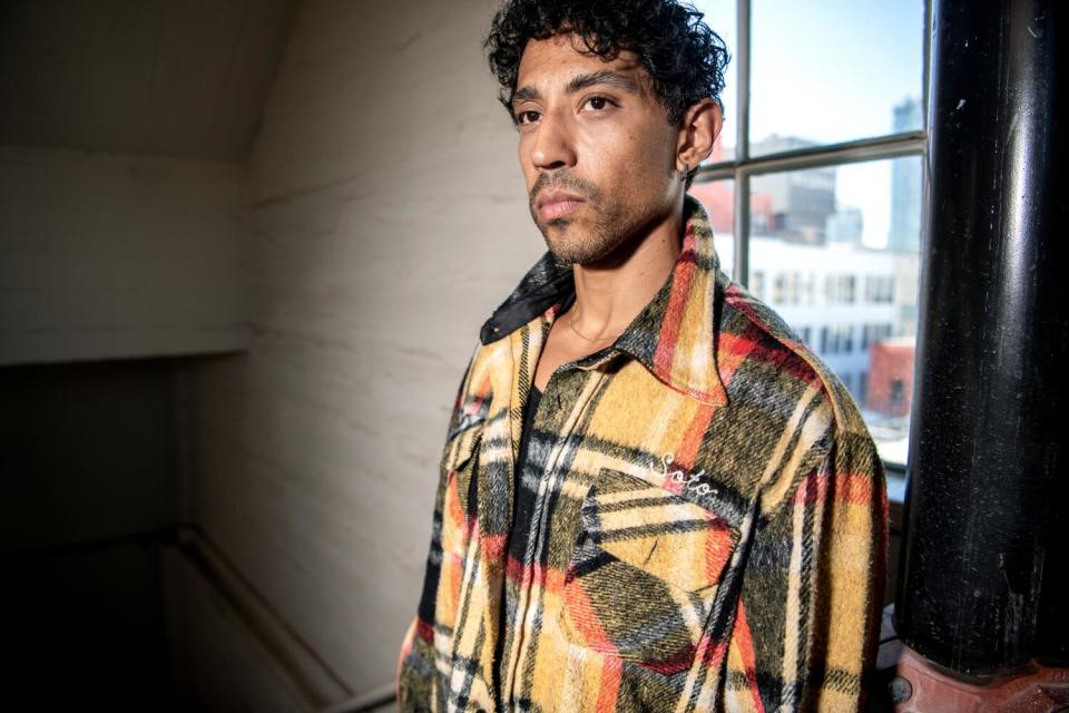 A man stands in a stairwell wearing a plaid yellow, green, and red jacket.