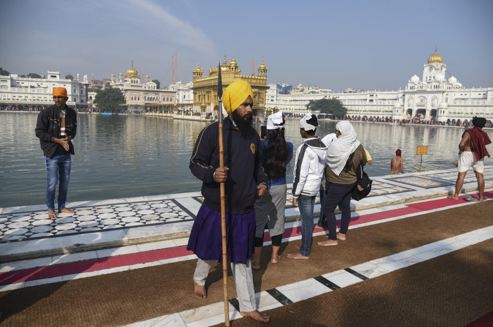 A Sikh guard stands holding a spear as devotees arrive to worship at the Golden Temple, one of Sikhs' most revered shrines in Amritsar, India, Sunday, Dec.19, 2021. A man was beaten to death Saturday after he allegedly attempted to commit a sacrilegious act inside the historic temple. (AP Photo/Prabhjot Gill)