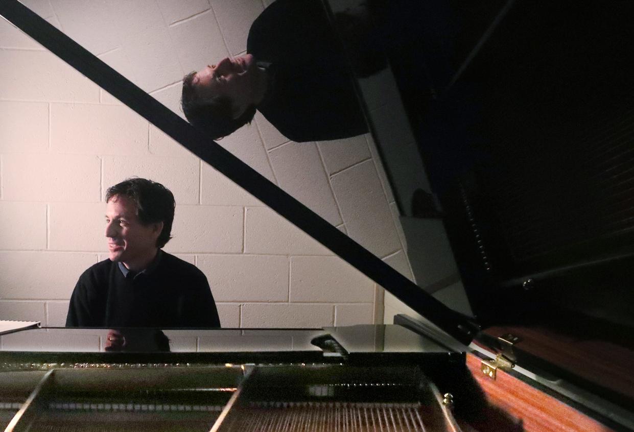 University of Akron professor James Wilding, reflected in the top of a baby grand piano, talks about his latest composition, "The Many Moods of Music," in Guzzetta Hall in Akron on Monday.