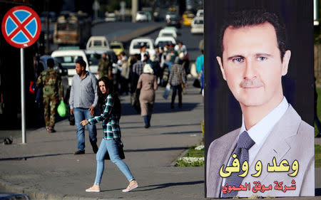 A woman walks near a picture of Syrian President Bashar al Assad in Damascus, Syria April 15, 2018. REUTERS/Ali Hashisho