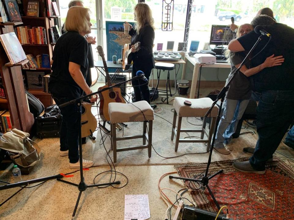 Old friends like John Tovar, and Vesper Sparrow’s Mary Karlzen (left), Kelly Christy (center) and Carolyn Colachicco (receiving the hug), prepare for their reunion set at My Mama’s Books & Records Records Cafe in Dania Beach on March 19, 2023.