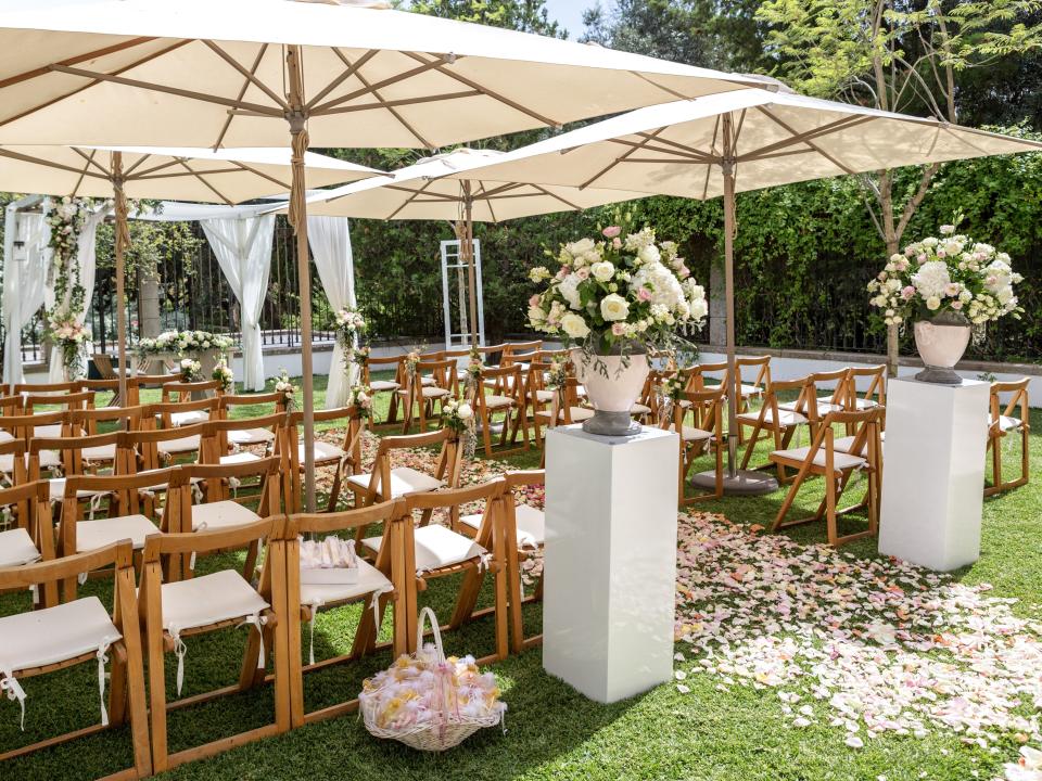 an outdoor wedding with flower petals down the aisle and umbrellas