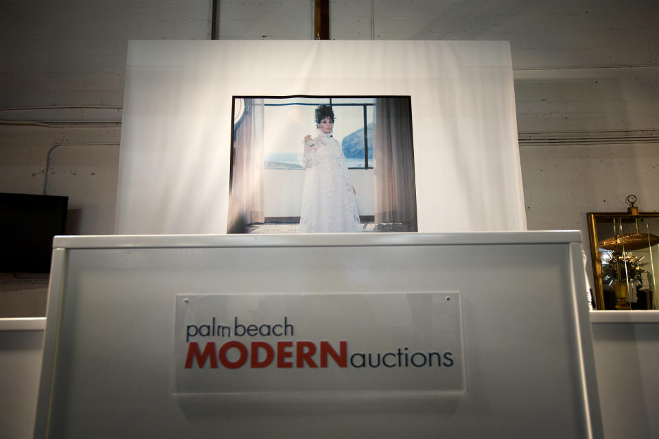 In this Monday, Dec. 30, 2013 photo, a photo of Elizabeth Taylor hangs over the auctioneer stands at an auction house in West Palm Beach, Fla. The signature of designer Karl Lagerfeld is adding an extra splash of glamour to a collection of fashion sketches up for auction in Florida. The half-century-old archive from the House of Tiziani in Rome will be sold Jan. 11, 2014, at Palm Beach Modern Auctions. (AP Photo/J Pat Carter)