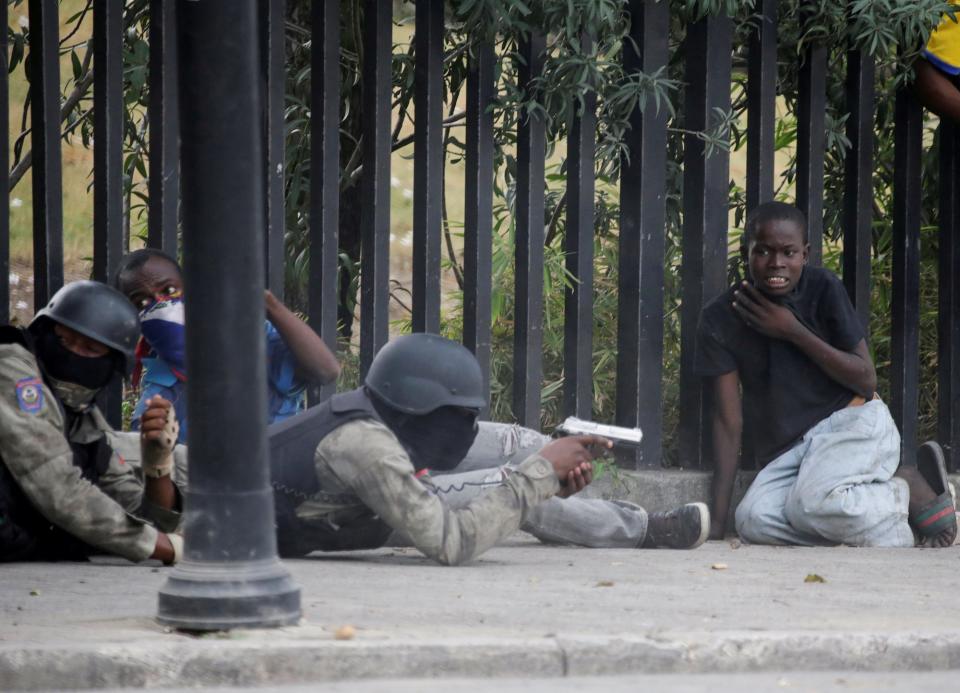 A boy gestures as a man in a Haitian National Police uniform aims a gun during a shooting in Champ de Mars, Port-au-Prince, Haiti February 23, 2020.